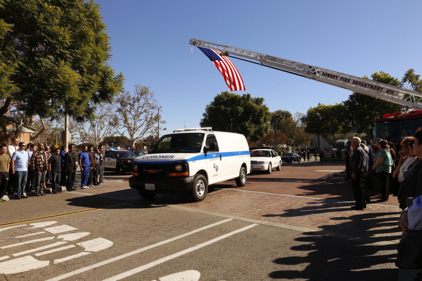 The body of Downey police Officer Ricardo Galvez is carried away in a coroner's van as onlookers line the streets outside the police department headquarters, where Galvez was found shot to death in his car.