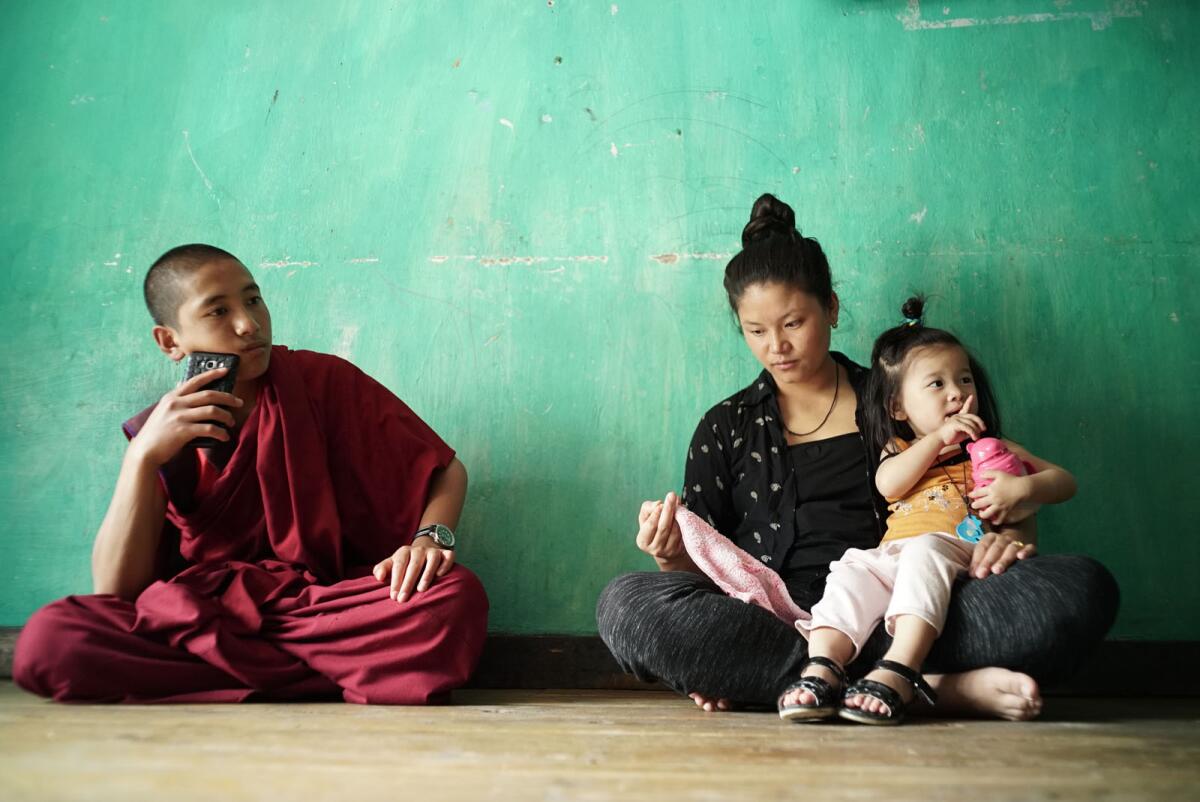 A young monk sits on the floor with a young mother and her daughter in the documentary "Sing Me a Song."