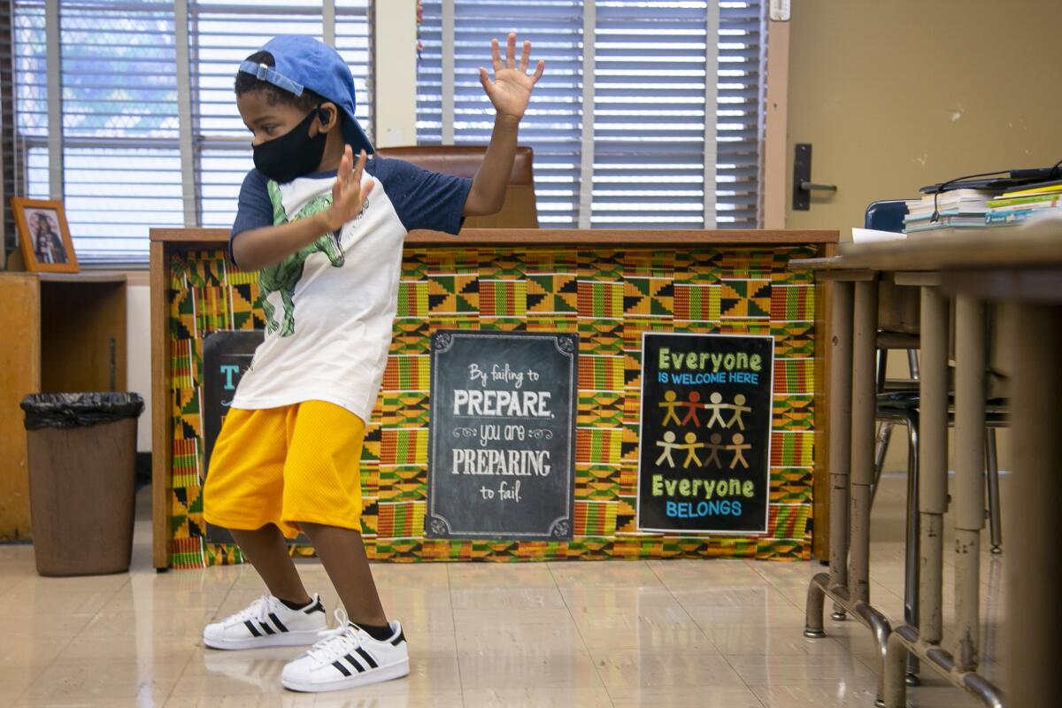 A young boy dances in front of a decorated teacher's desk in a schoolroom 