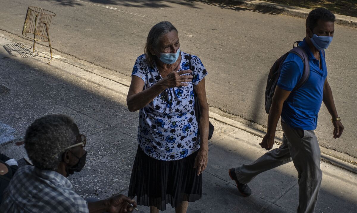 People wearing masks as a precaution amid the new coronavirus pandemic speak on the street as they wait to enter a COVID-19 vaccination center set up inside a cultural center in Havana, Cuba, Monday, Aug. 2, 2021. (AP Photo/Ramon Espinosa)