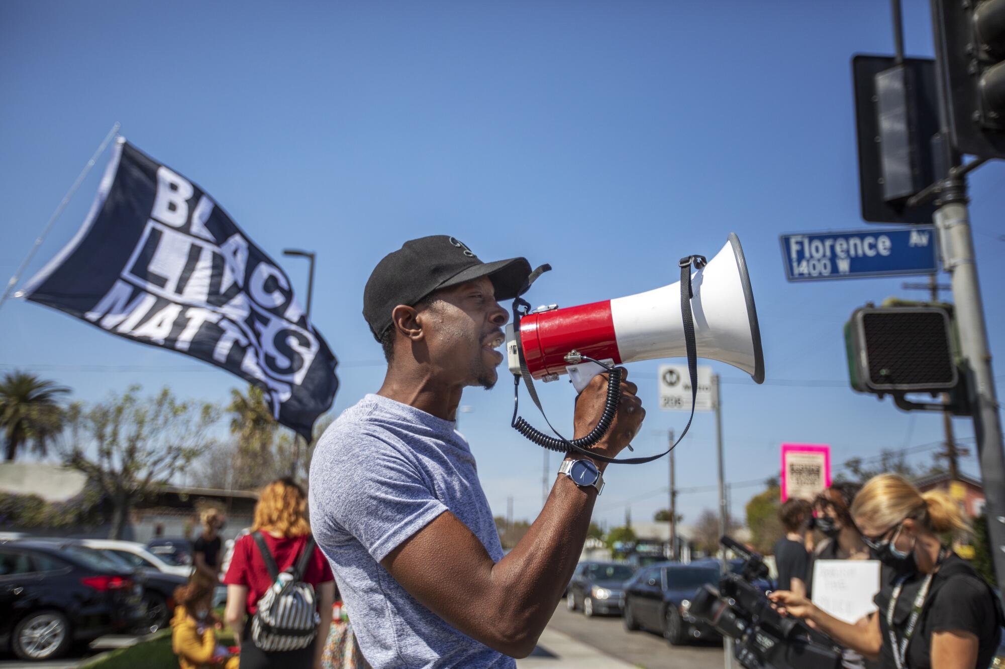 A man speaks into a megaphone in front of a Black Lives Matter flag 