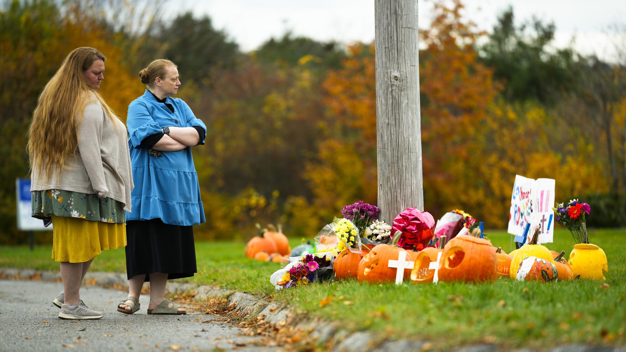 Two people stand next to a makeshift memorial of pumpkins, crosses, flowers and signs