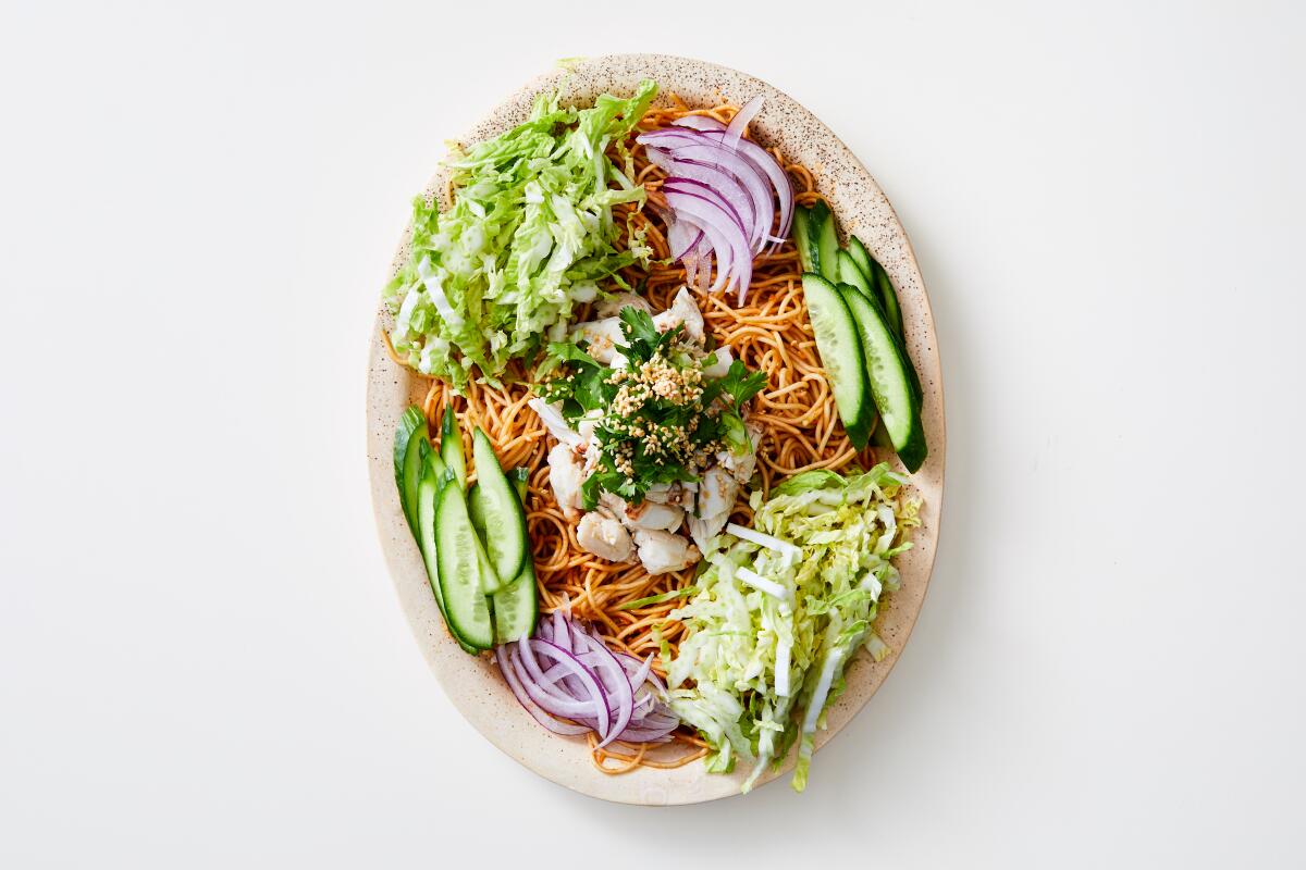 A bowl of noodles with crab meat, cucumbers, shredded cabbage and scallions