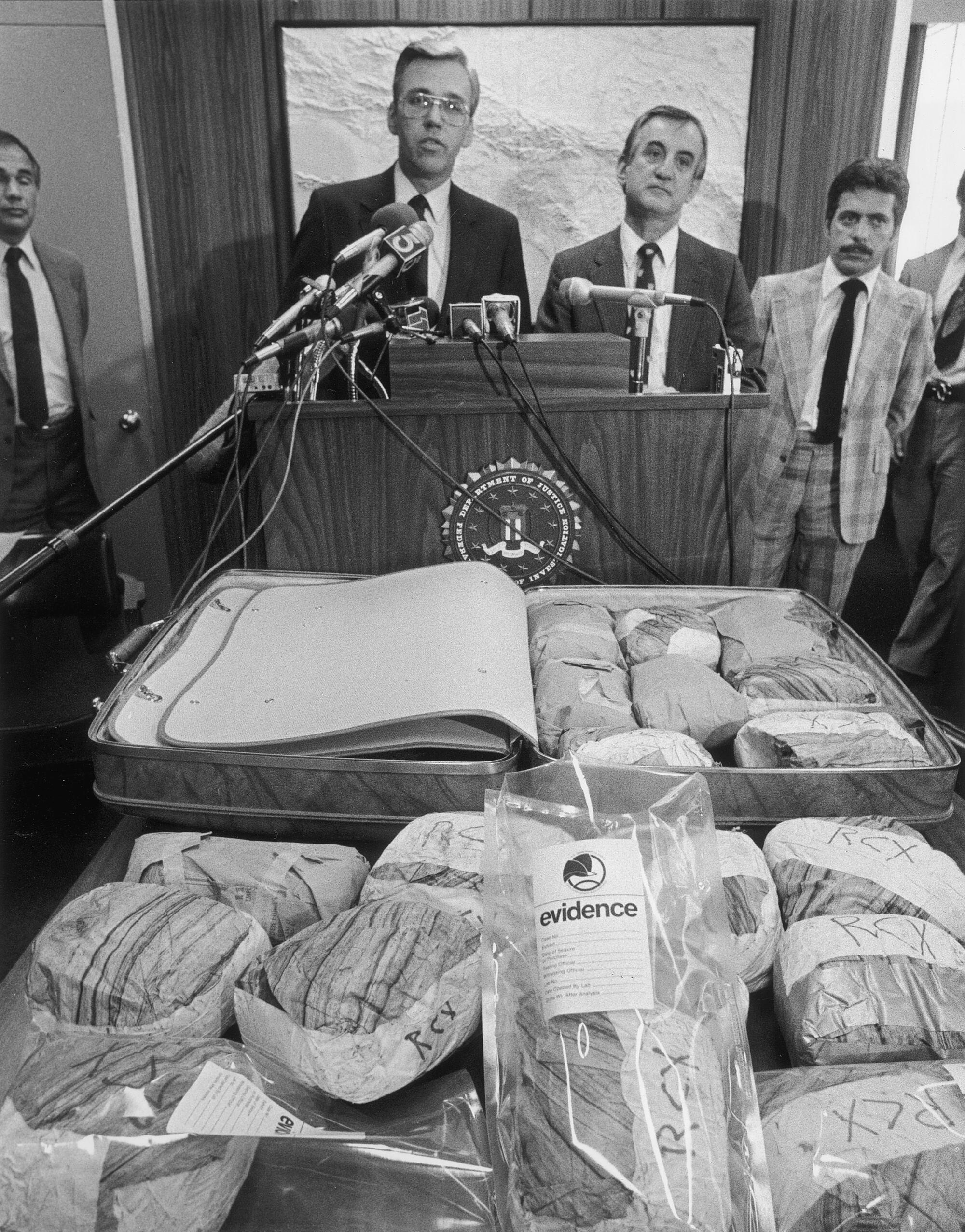 People are standing behind a lectern, with packages on a table in front of them.