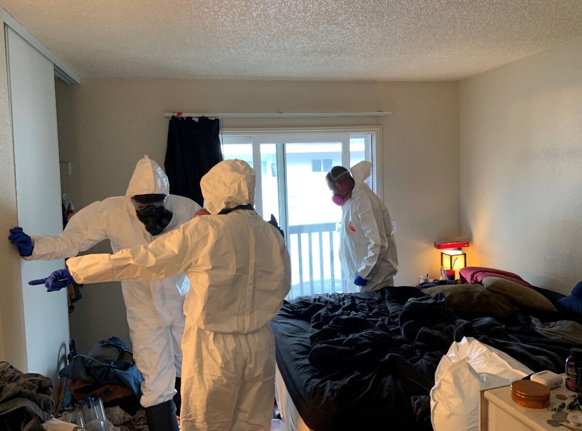 Three people in hazmat suits in a bedroom