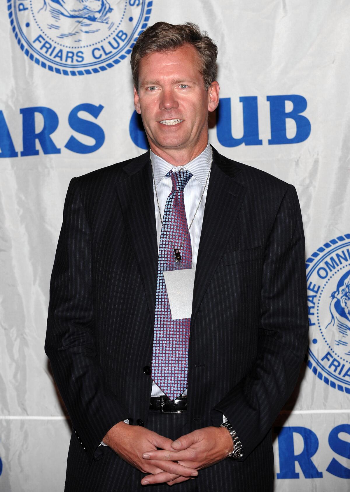 A man posing in a black suit and geometric tie