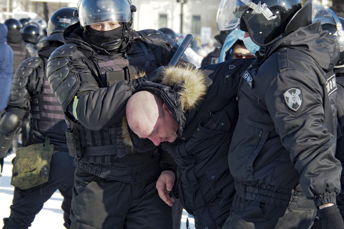 Helmeted police, one holding a baton, stand over a man whom they've bent over.