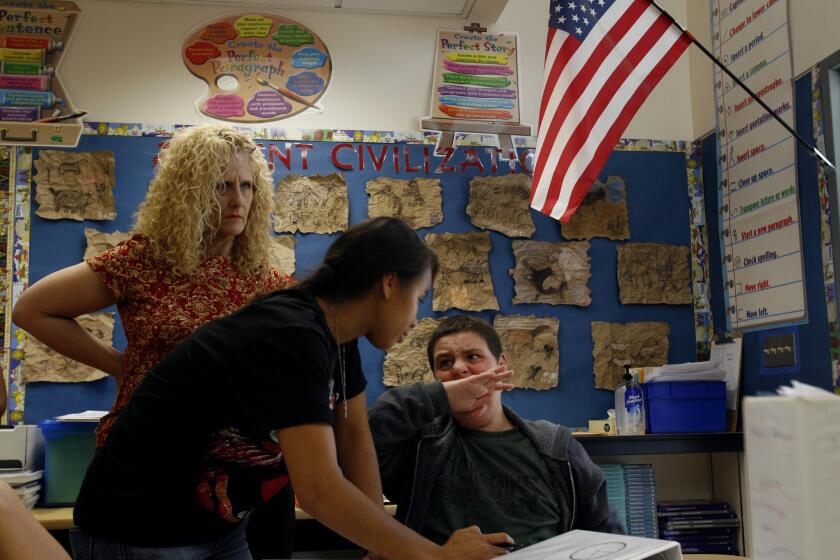 Behavior specialist Michelle May tries to calm down 13-year-old Jonah Funk after he starts biting his hand while working with Sarabeth Rothfeld, in back, at Hesby Oaks School in Encino.