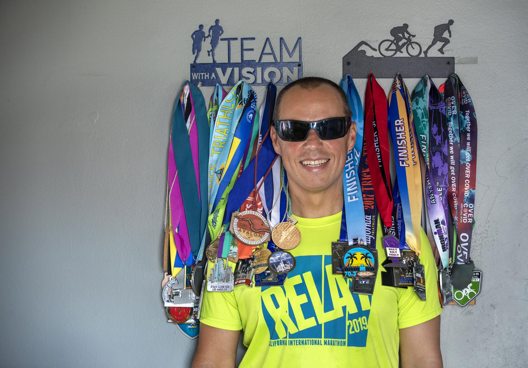 Tony Duenas stands in his L.A. home in front of medals he has won competing in marathons, ultra marathons and triathlons. 
