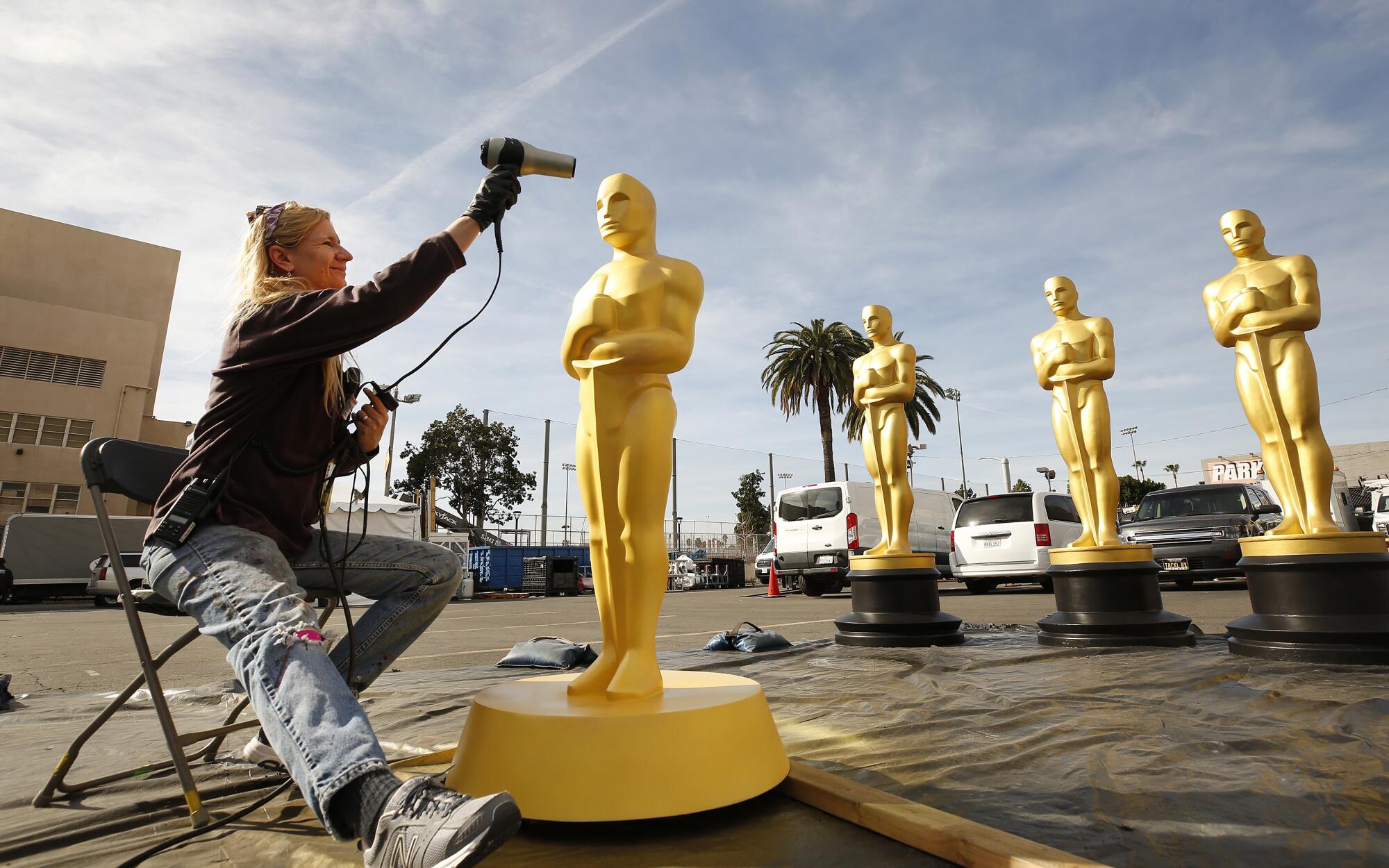 Scenic artist Dena D’Angelo dries freshly painted Oscar statues
