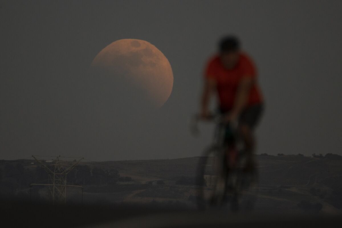 A lunar eclipse is seen behind a cyclist during the first blood moon of the year, in Irwindale, Calif., Sunday, May 15, 2022. (AP Photo/Ringo H.W. Chiu)