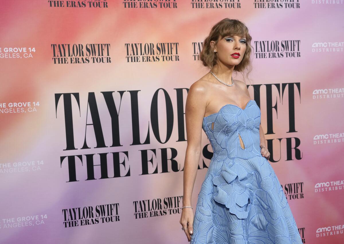 Taylor Swift poses in a light blue strapless dress against a pink backdrop