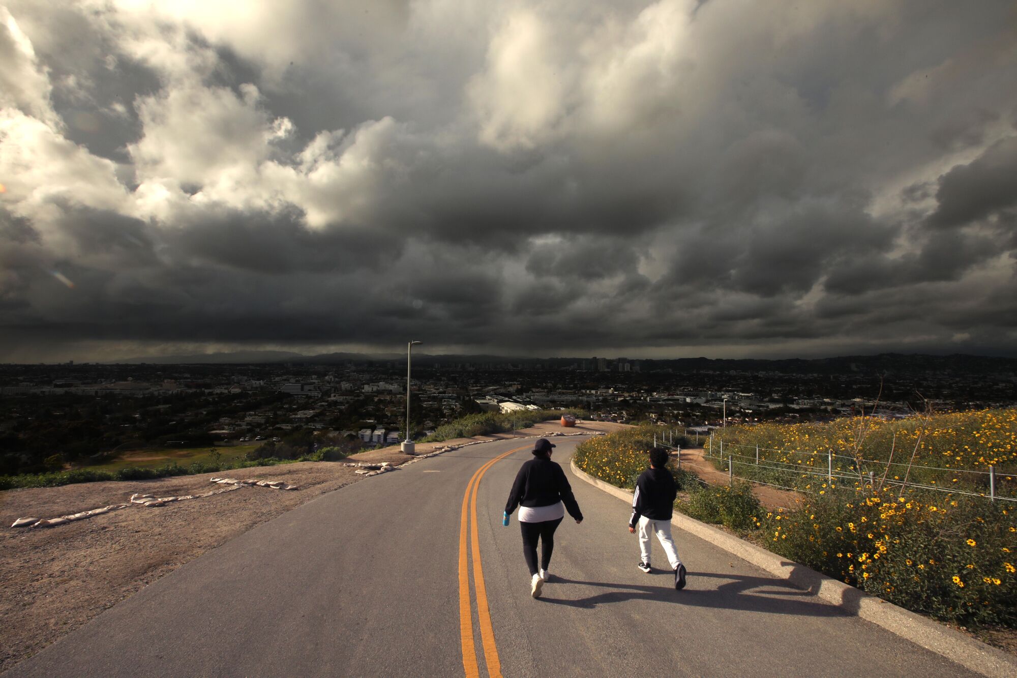 Walking down a two-way street, a pair of walkers make their way toward the darkness of rain clouds 