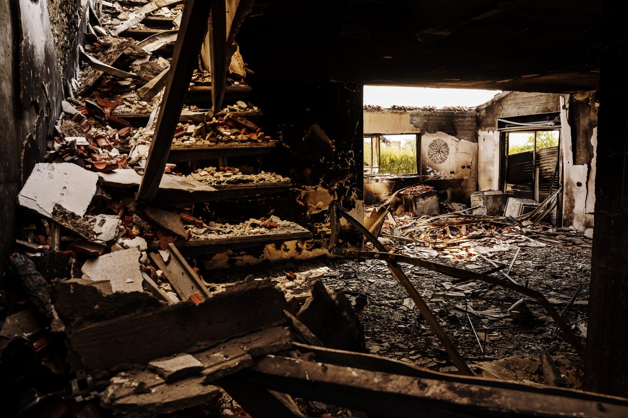Debris covering stairs and the floor of a scorched house with roof and windows blown out