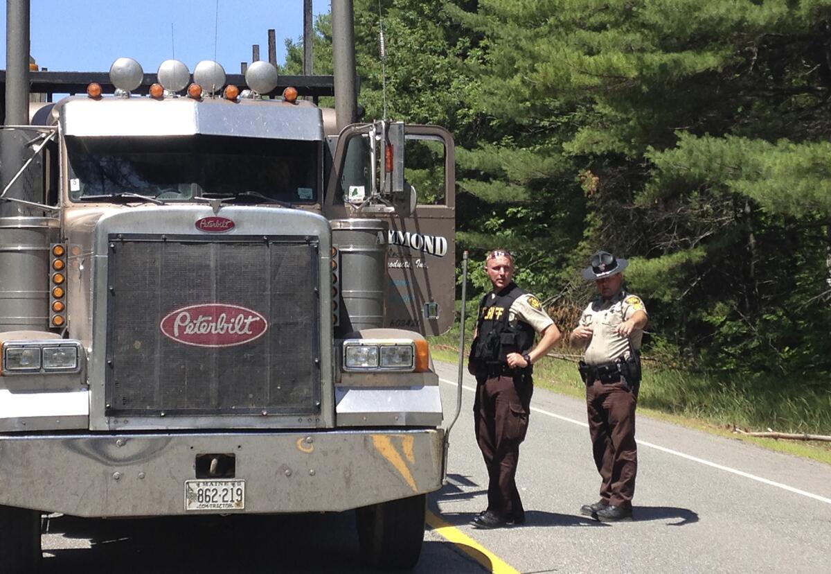 Oficiales del condado de Penobscot hablan con el chofer de camión en un punto de revisión el 17 de julio de 2015 en Lee, Maine. La policía buscaba a un pistolero en un camión maderero robado después de dispararle a cuatro personas durante la noche en los pueblos de Lee, Benedicta y Silver Ridge al norte de Maine. (Foto AP/Alanna Durkin)