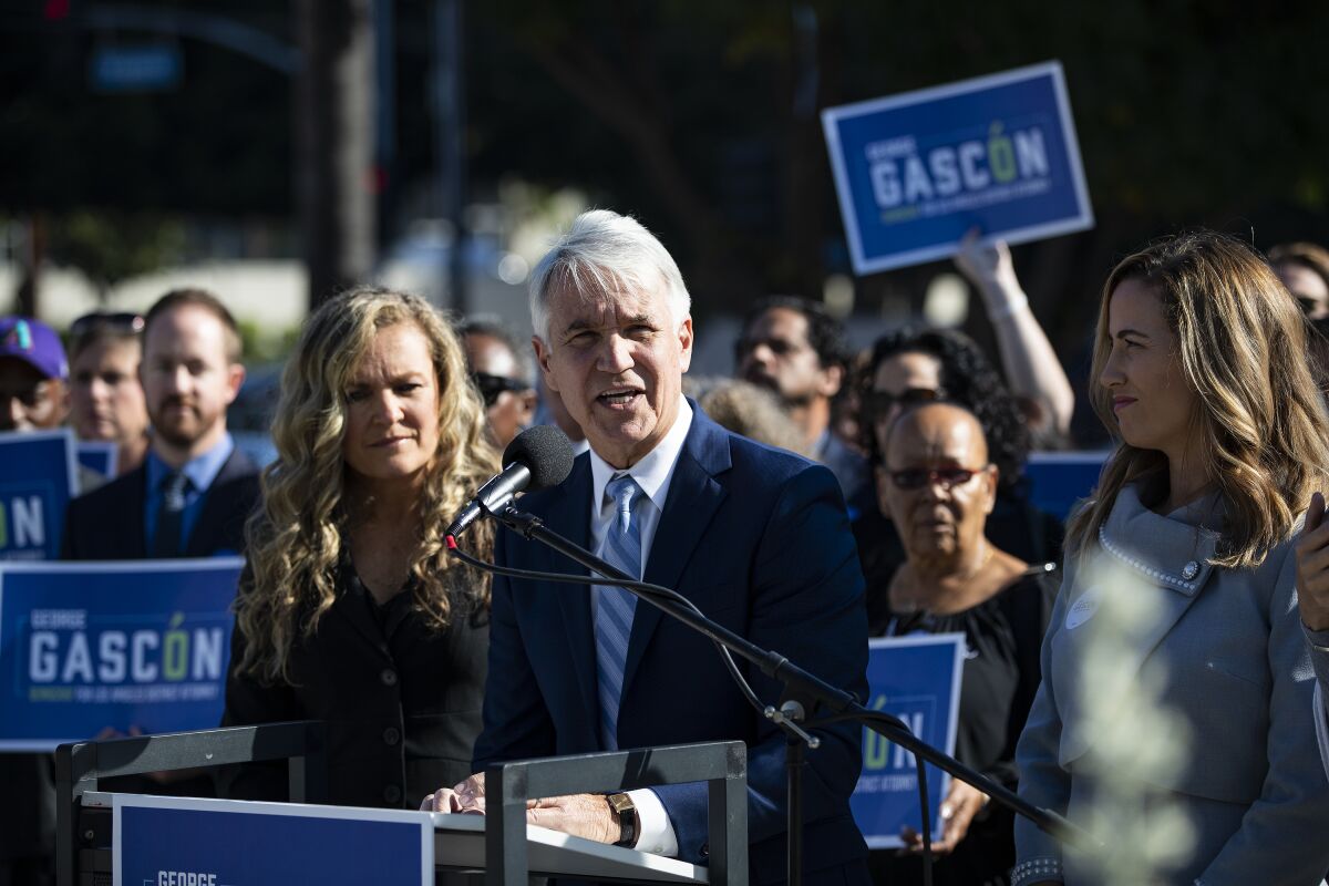 George Gascón speaks at a lectern in front of a crowd of people holding his blue campaign signs