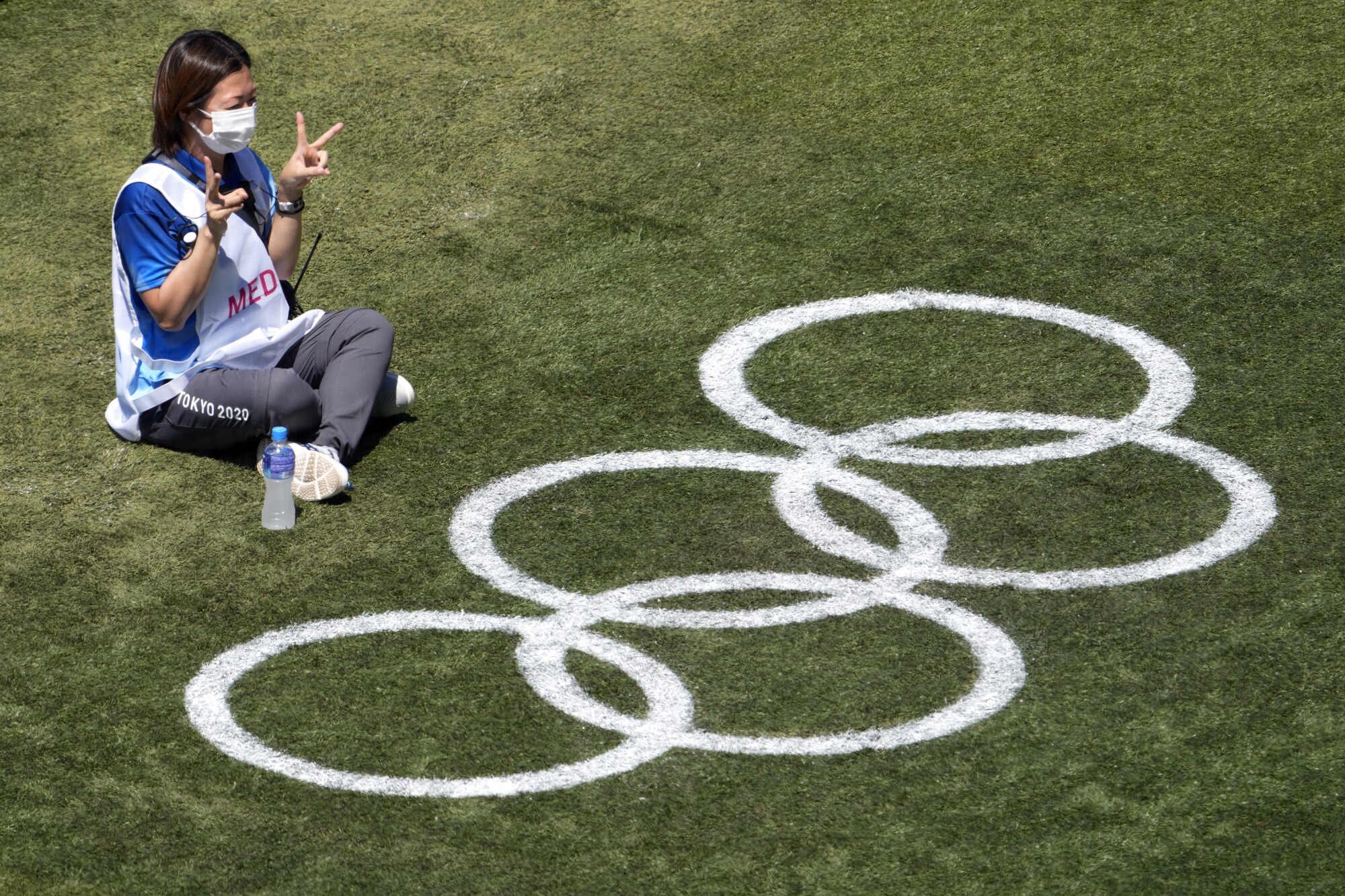A worker poses with Olympic rings on grass 