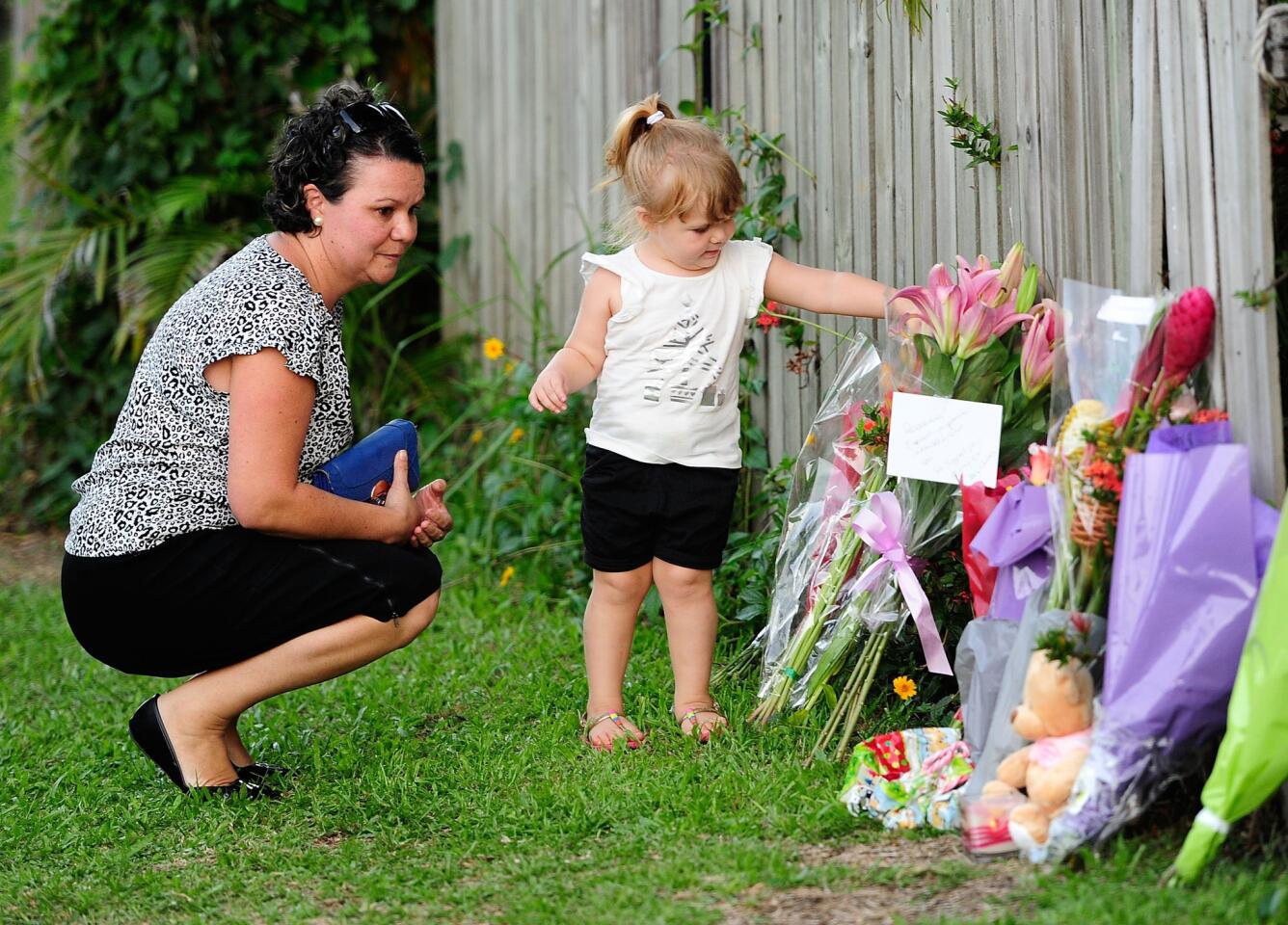 A woman and child lay flowers across the road from a home where eight children were found dead in the Cairns suburb of Manoora, Australia.