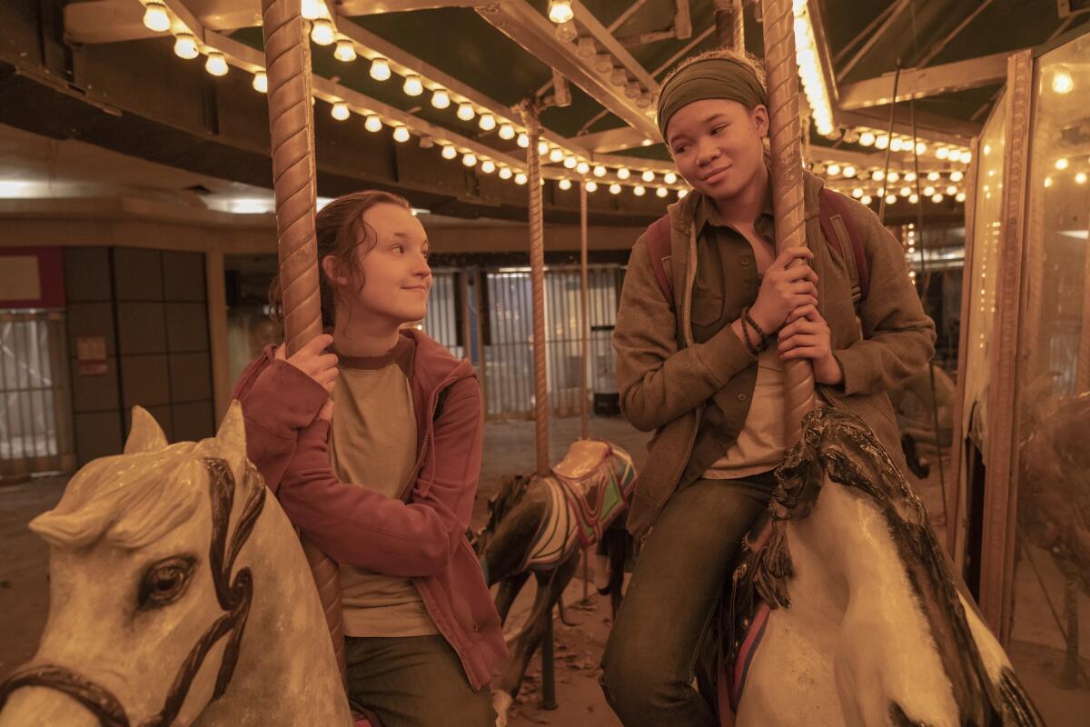 Two girls ride horses on a carousel.