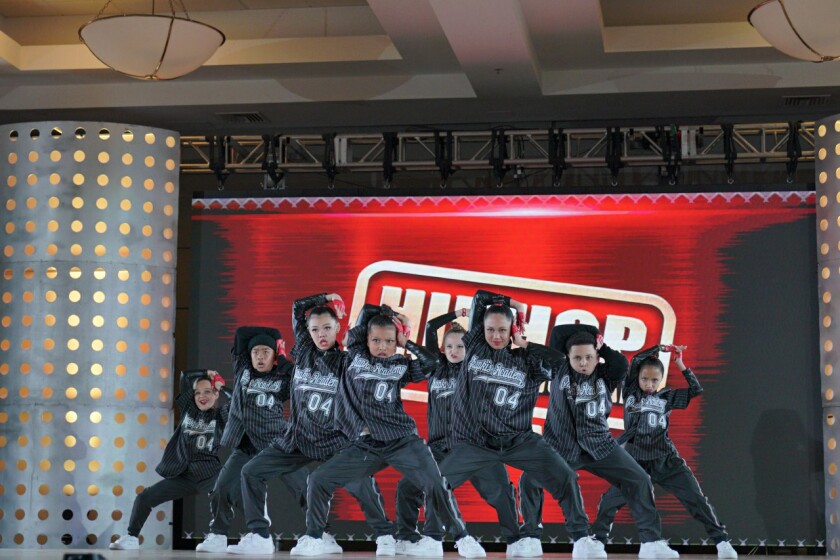 A hip-hop dance crew of youngsters dressed in black on a stage.