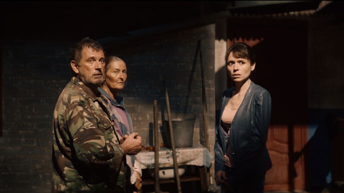 A man in camouflage and two women stand in a darkened room.