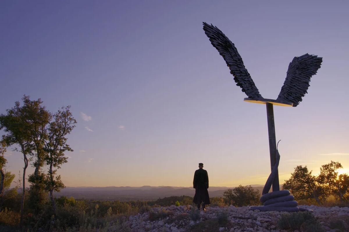 A person stands by a large outdoor sculpture of wings.