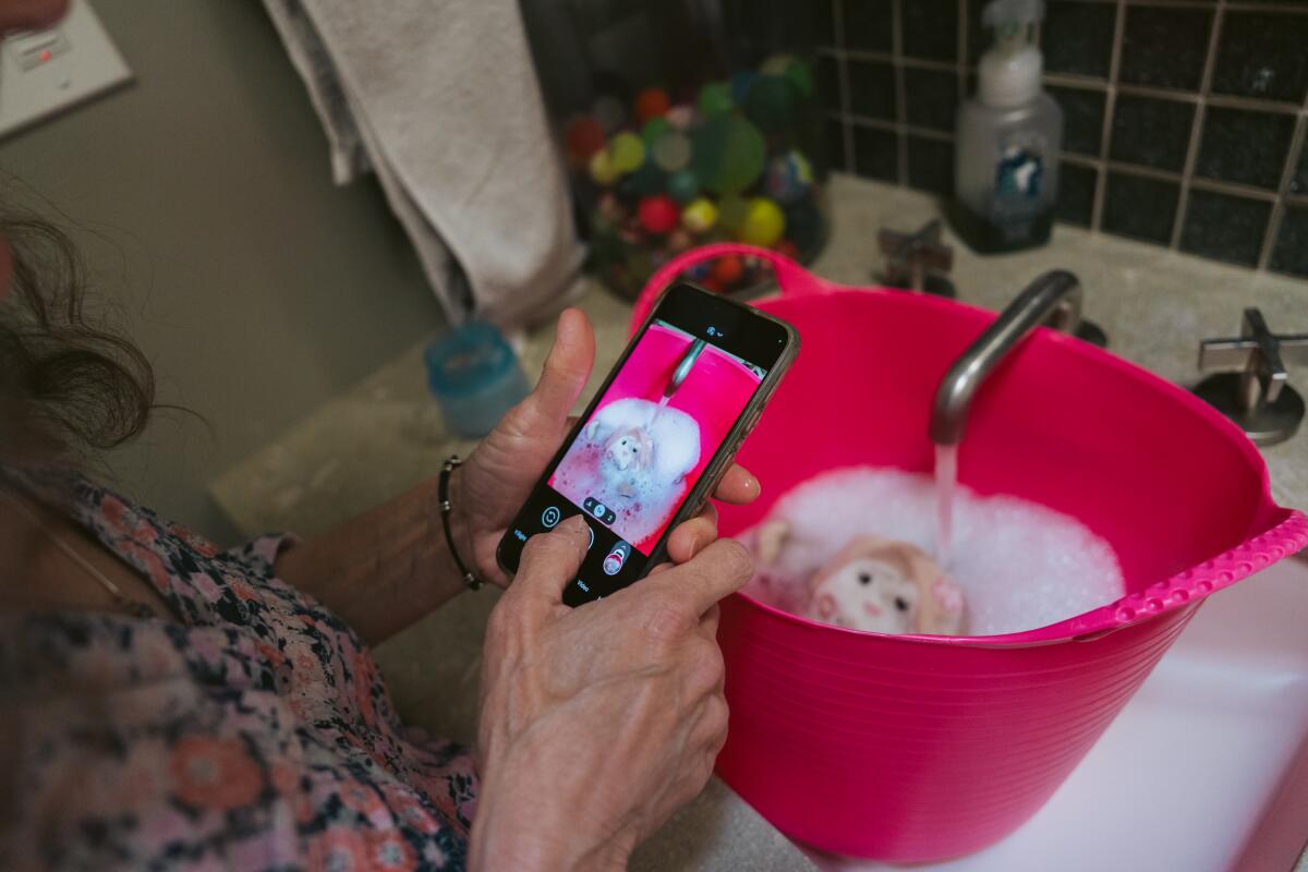 A woman takes a photo of a toy sitting in a tub of sudsy water.