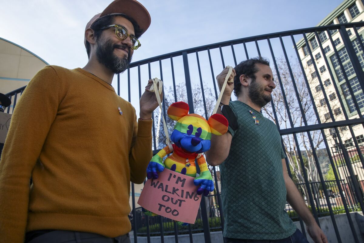 Disney employees Carlos Lopez Estrada, left, and Juan Pablo Reyes hold a rainbow Mickey Mouse doll.