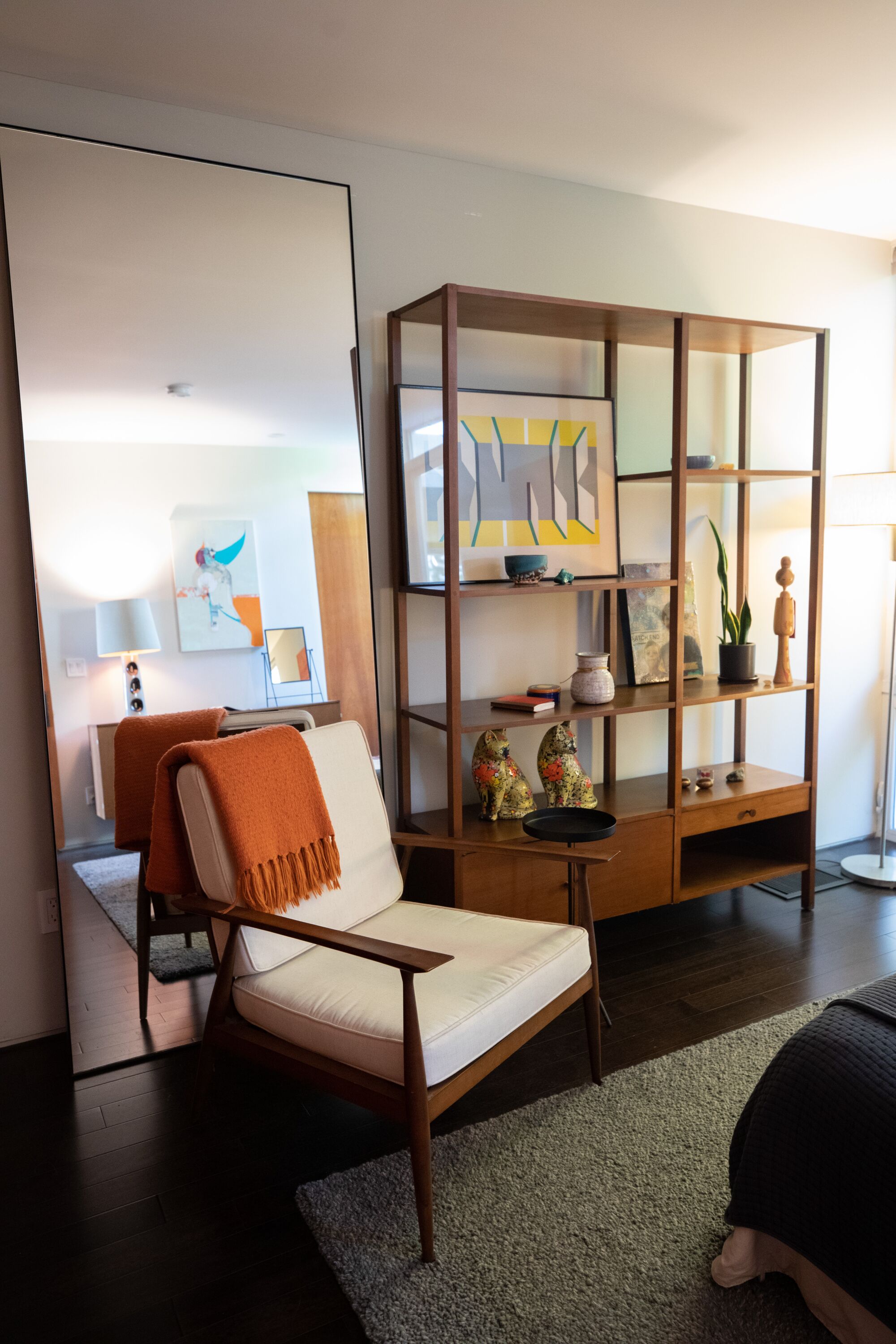 A Modernist easy chair upholstered in white sits before a backless wooden shelf in a bedroom