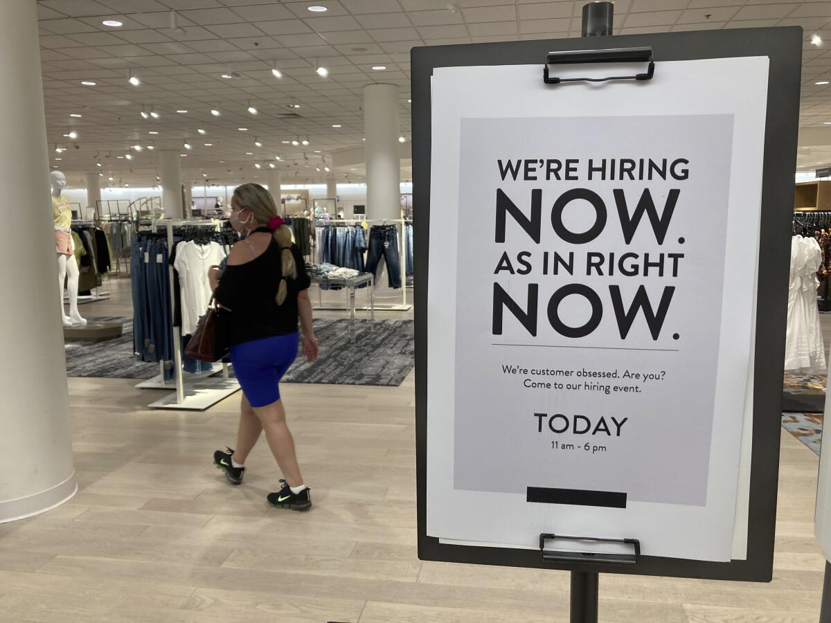 Inside a high-end department store, a sign reads "We're hiring now. As in right now." 