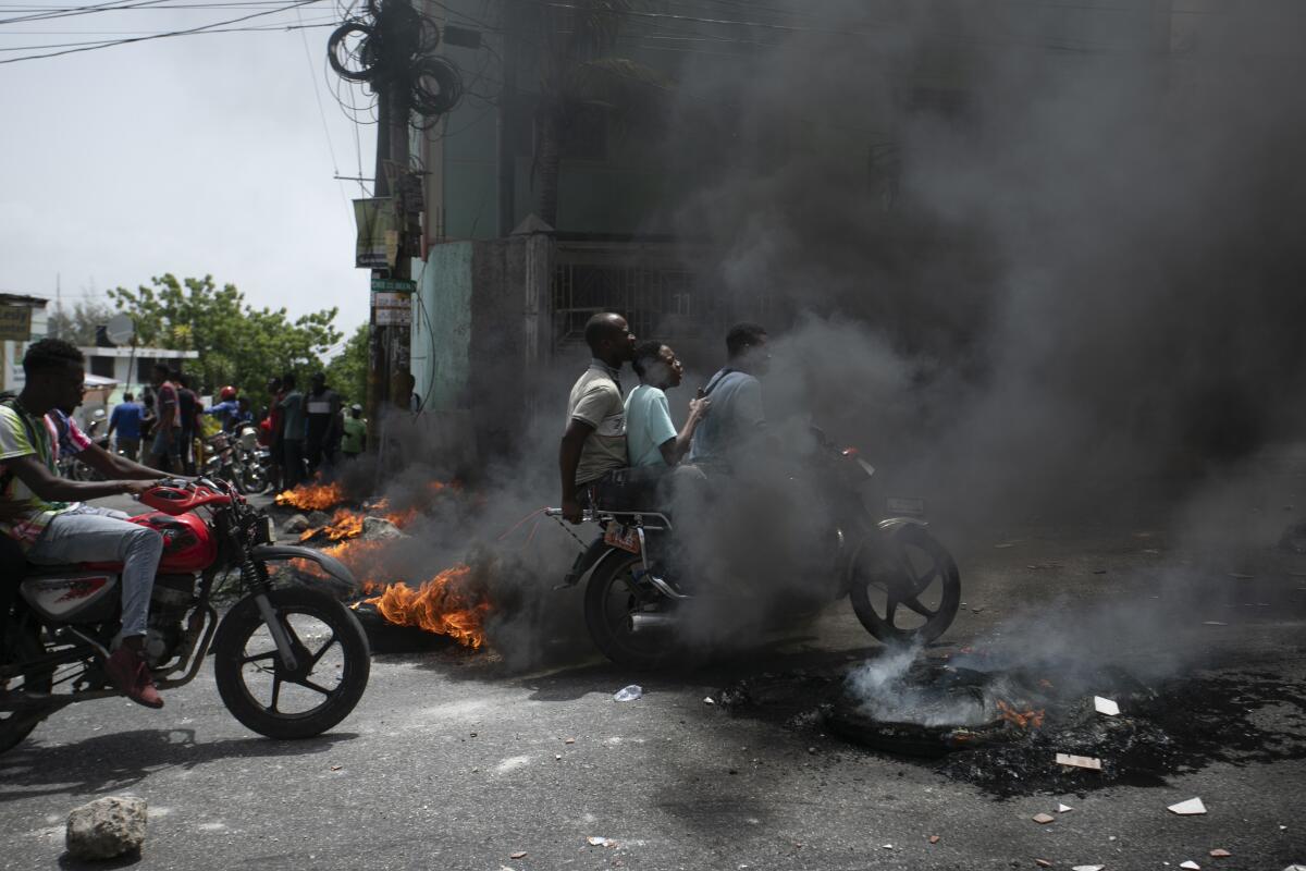 El conductor de un mototaxi lleva a sus clientes frente a una barricada en llamas colocada por taxistas 