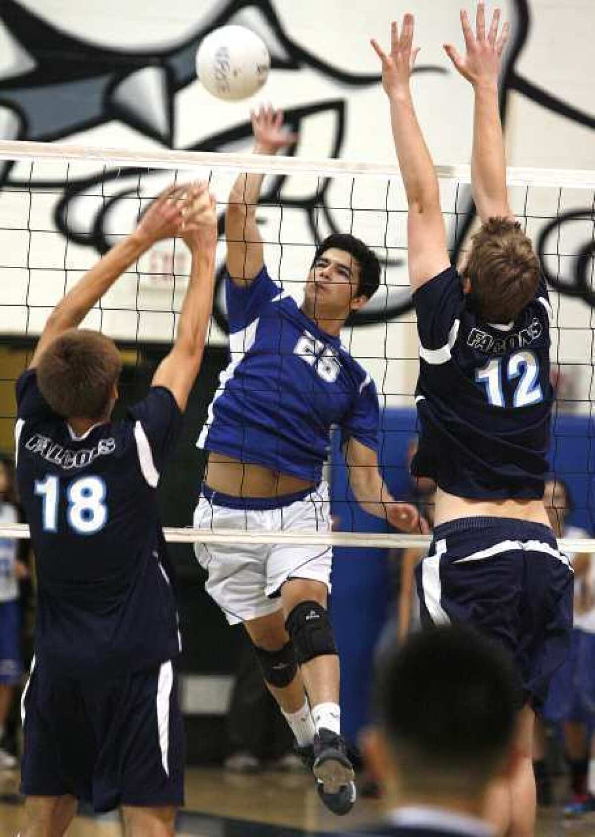 Burbank's Derian Blandon spikes a kill attempt over the defense of Crescenta Valley's Freedom Tripp and Zachary Burch in a Pacific League boys volleyball match.