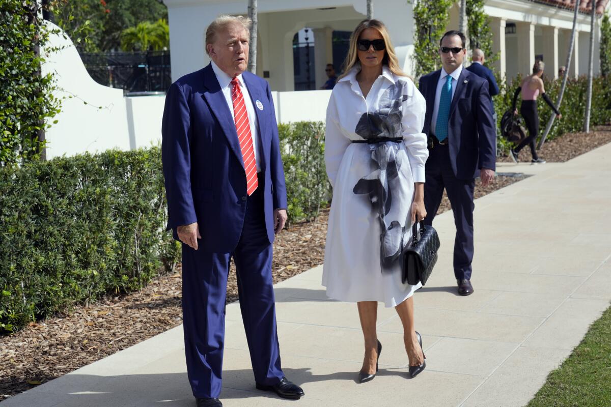 Former President Trump stands on a sidewalk with Melania Trump.