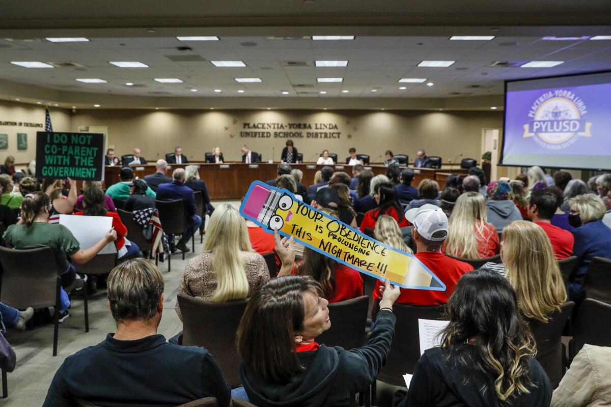 People at a school board meeting hold signs including "I Do Not Co-Parent With The Government."