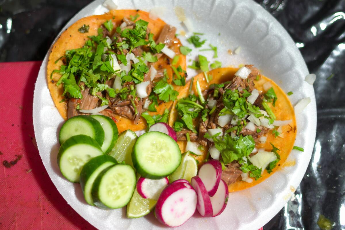 Open-face tacos on a paper plate with slices of radish and cucumber and lime wedges