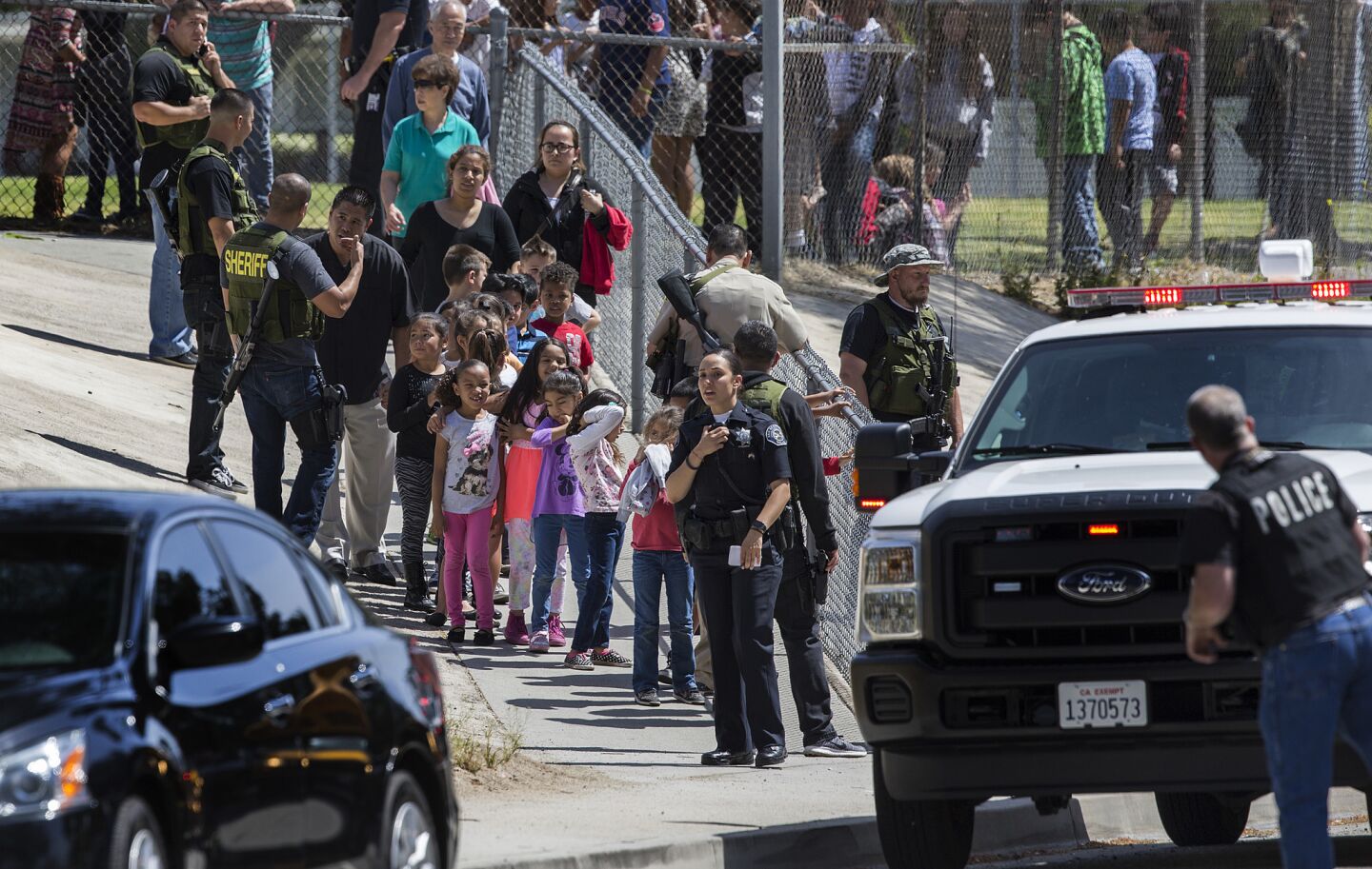 San Bernardino police officers help evacuate children to awaiting school buses after a shooting inside North Park Elementary School in San Bernardino.