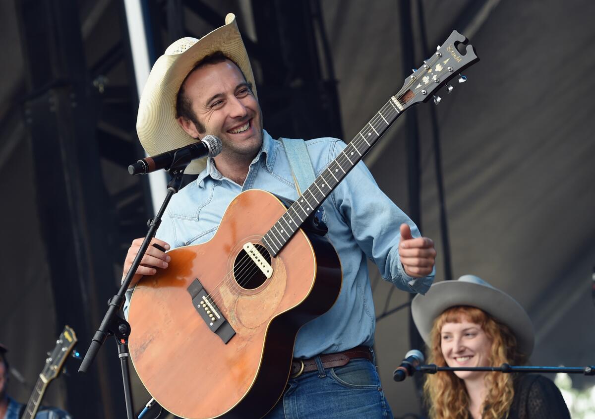 A man holding a guitar smiles while standing in front of a microphone