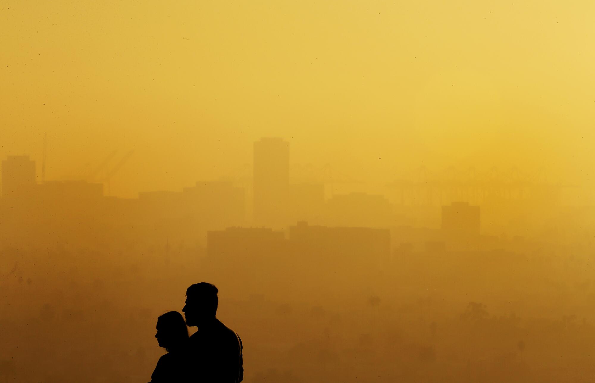 Two people silhouetted against smoggy downtown Long Beach.