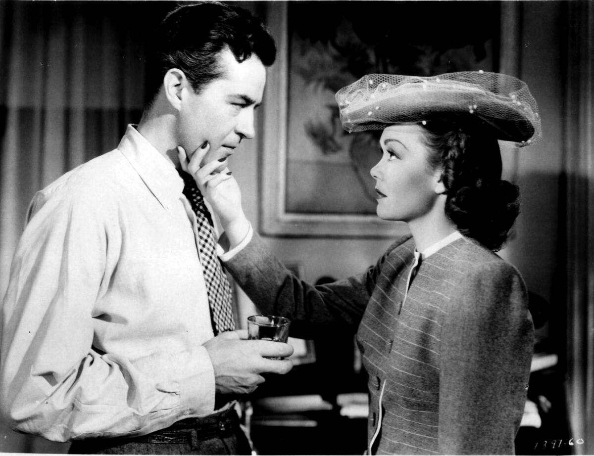 A black-and-white photo of a woman with her hand cupping a man's chin as they stand face to face. He holds a drink. 