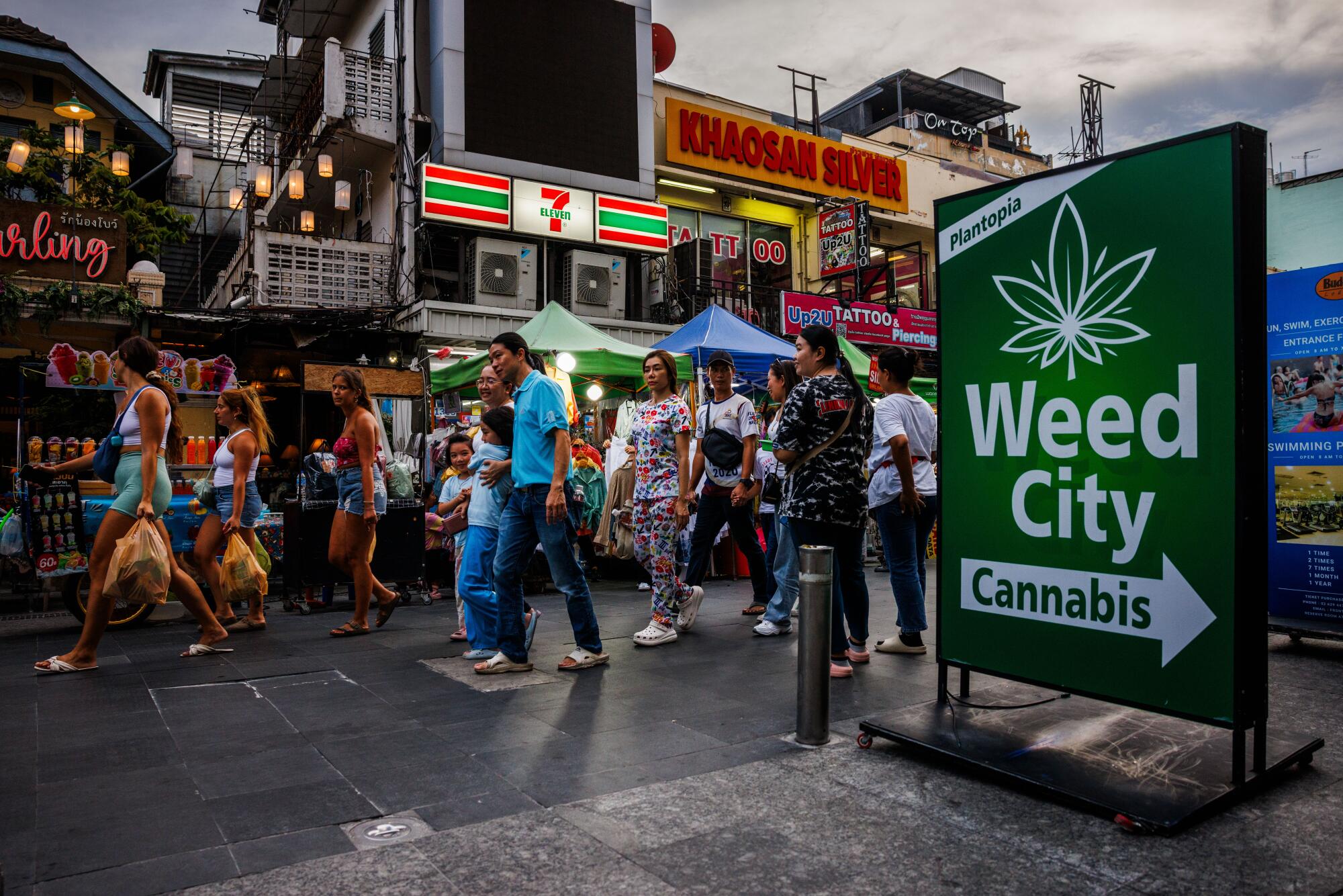 People walk past storefronts and a green sign that says Weed City