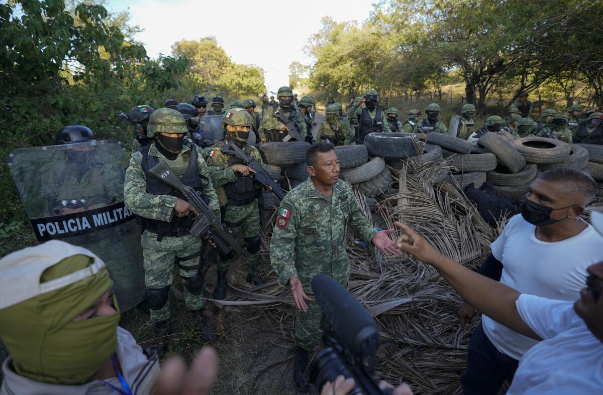 FILE - Residents who are fed up with the army's strategy of simply separating the Jalisco and the Michoacan-based Viagras gangs, confront Mexican soldiers taking cover behind a barricade of car tires, in Loma Blanca, Mexico, Tuesday, Nov. 16, 2021. Mexico's Supreme Court upheld on Tuesday, Nov. 29, 2022, a constitutional change that allows the military to continue in law enforcement duties until 2028. (AP Photo/Eduardo Verdugo, File)
