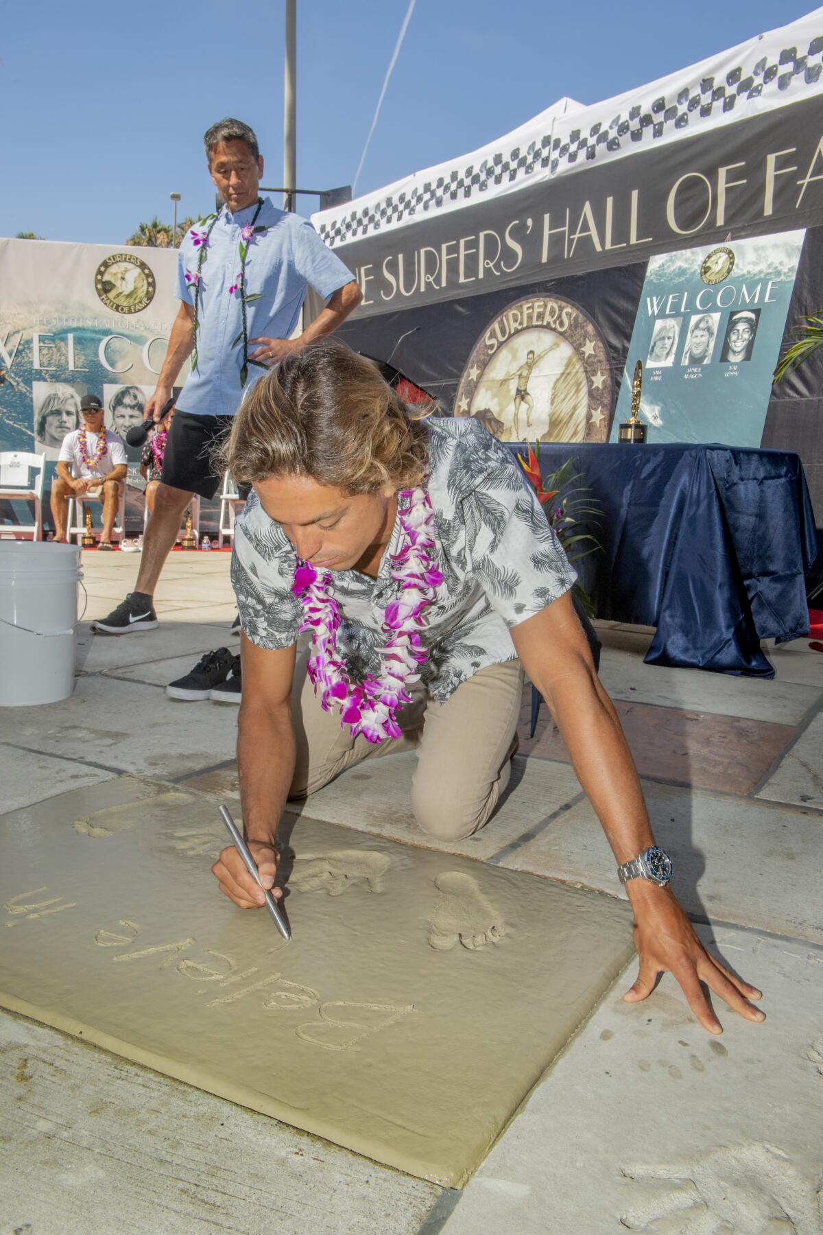 Kai Lenny, an all-around water sports athlete, writes "Believe in yourself" in wet cement Friday during his induction to the Surfers' Hall of Fame in Huntington Beach.