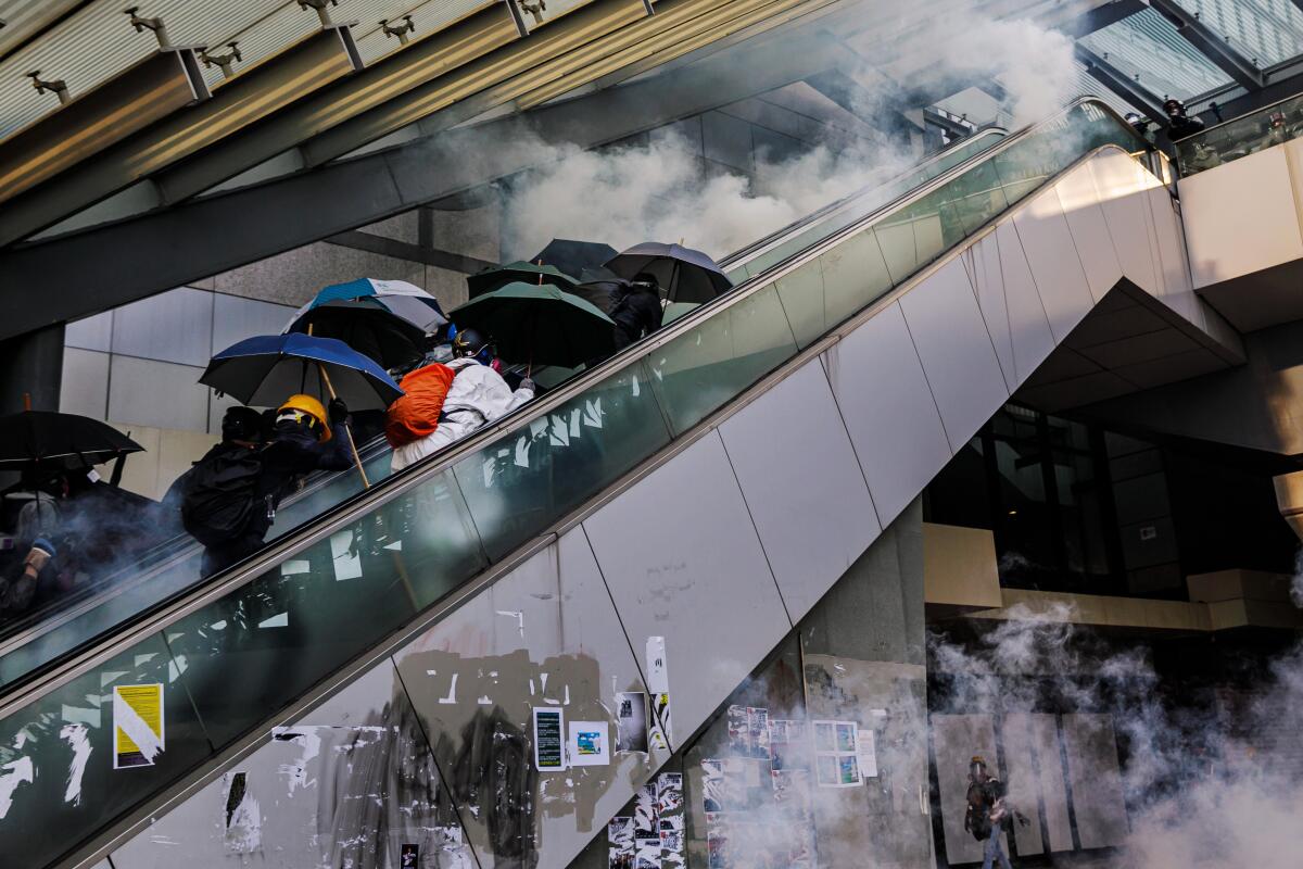 Pro-democracy demonstrators charge up a pair of escalators where police officers are making their stand, as a barrage of tear gas canisters and rubber bullets rain down on them.