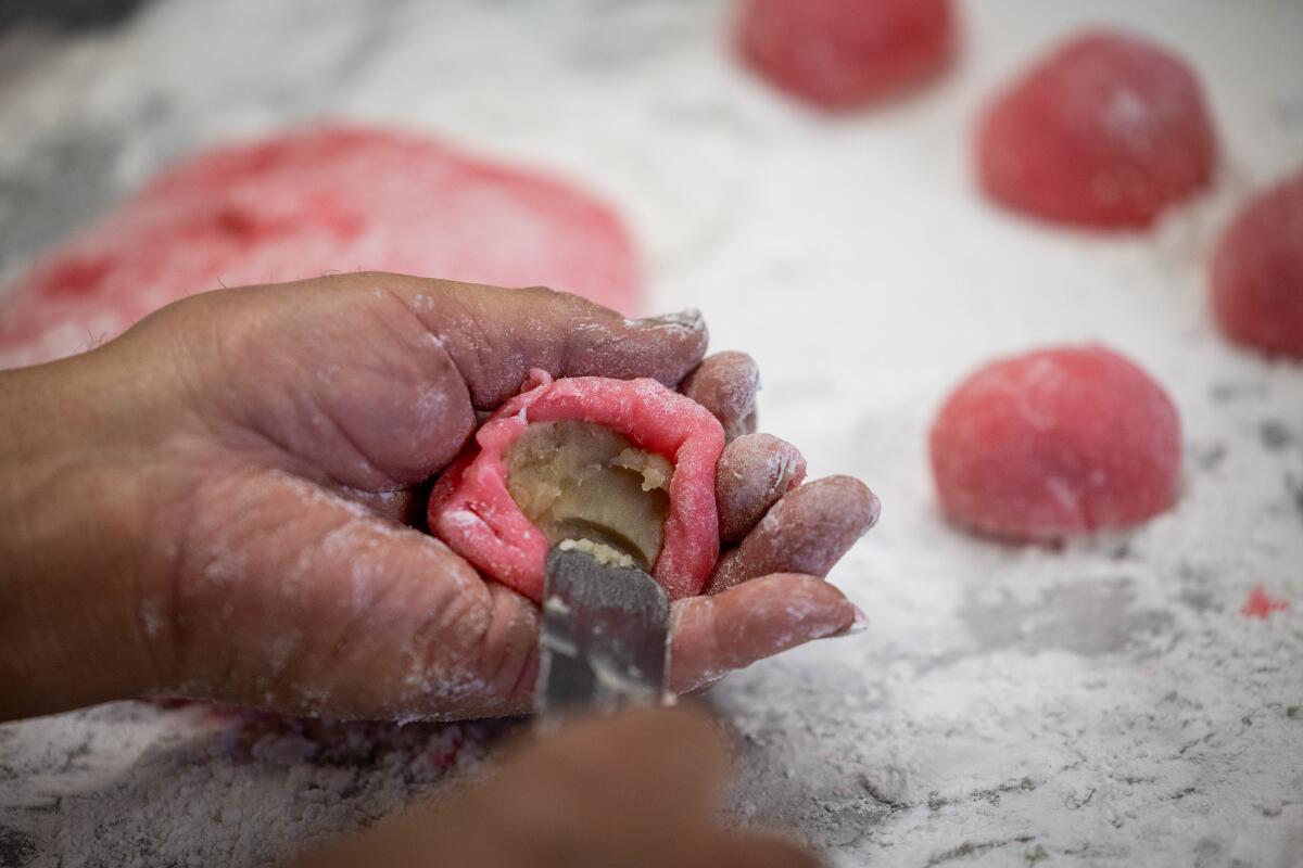 A close-up of Mas Fujita's hands using an icing spatula to mix white bean into pink mochi over a flour-dusted surface