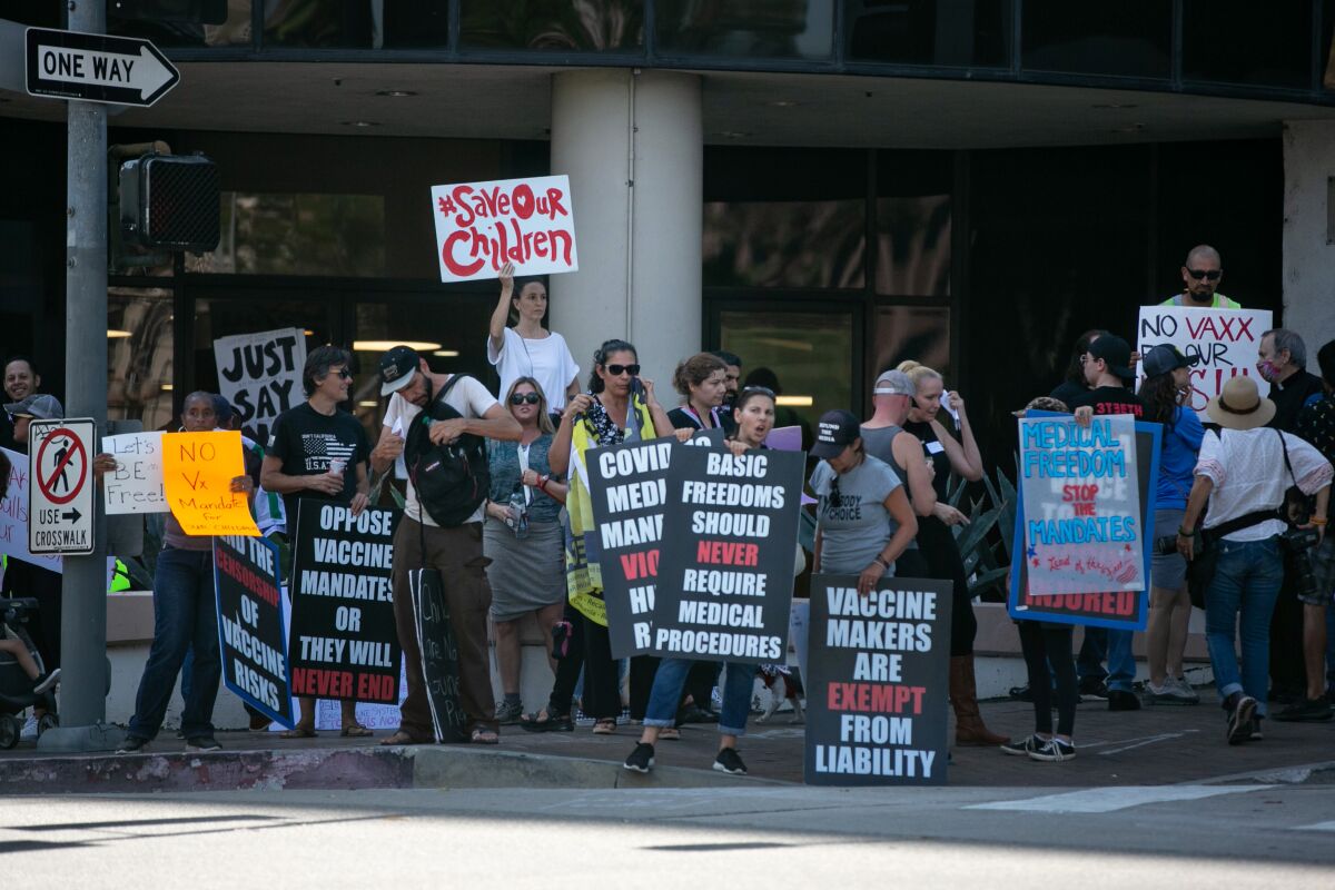 People stand on a street corner holding signs against vaccine mandates.