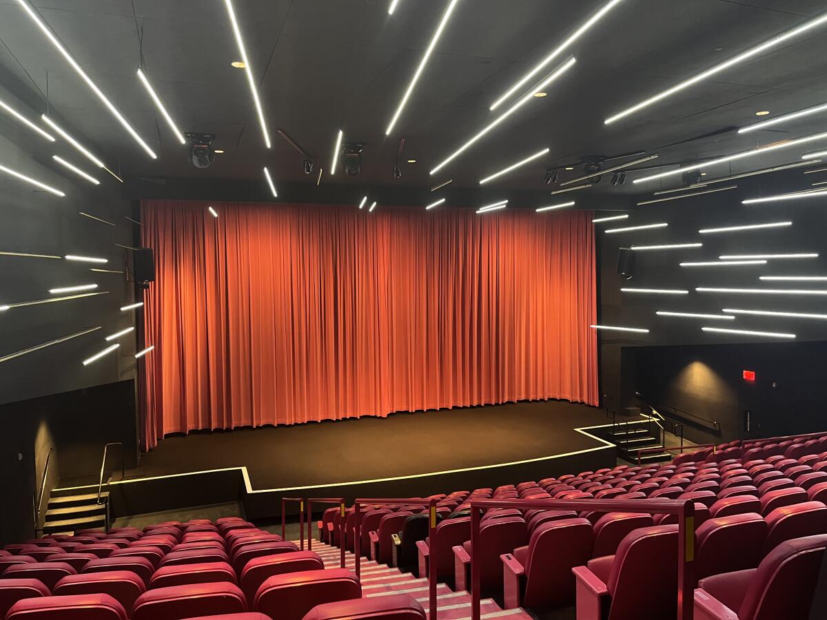 In a theater, a movie screen covered in velvety red curtains is framed by an abstract pattern of neon light