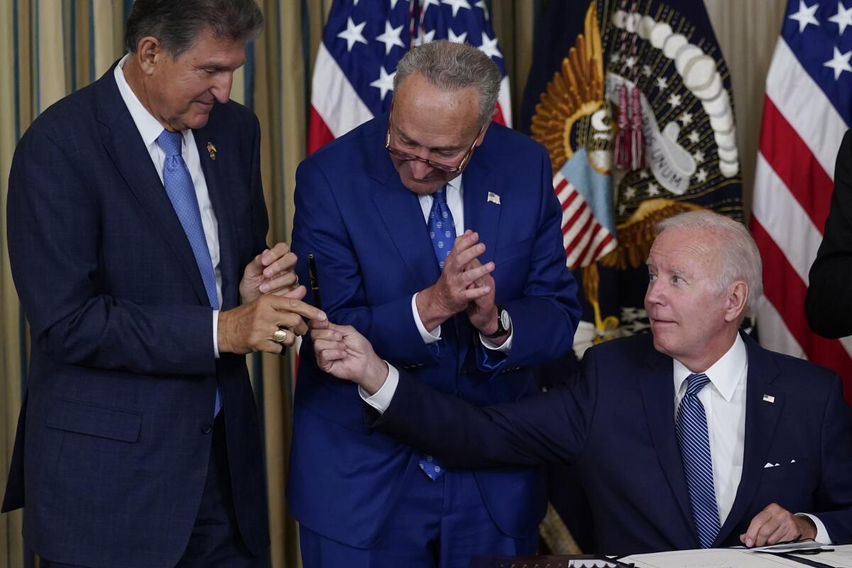FILE - President Joe Biden hands the pen he used to sign the Democrats' landmark climate change and health care bill to Sen. Joe Manchin, D-W.Va., as Senate Majority Leader Chuck Schumer of N.Y., watches in the State Dining Room of the White House in Washington, Aug. 16, 2022. Manchin made a deal with Democratic leaders as part of his vote pushing the party's highest legislative priority across the finish line last month. Now, he's ready to collect. But many environmental advocacy groups and lawmakers are balking. (AP Photo/Susan Walsh, File)