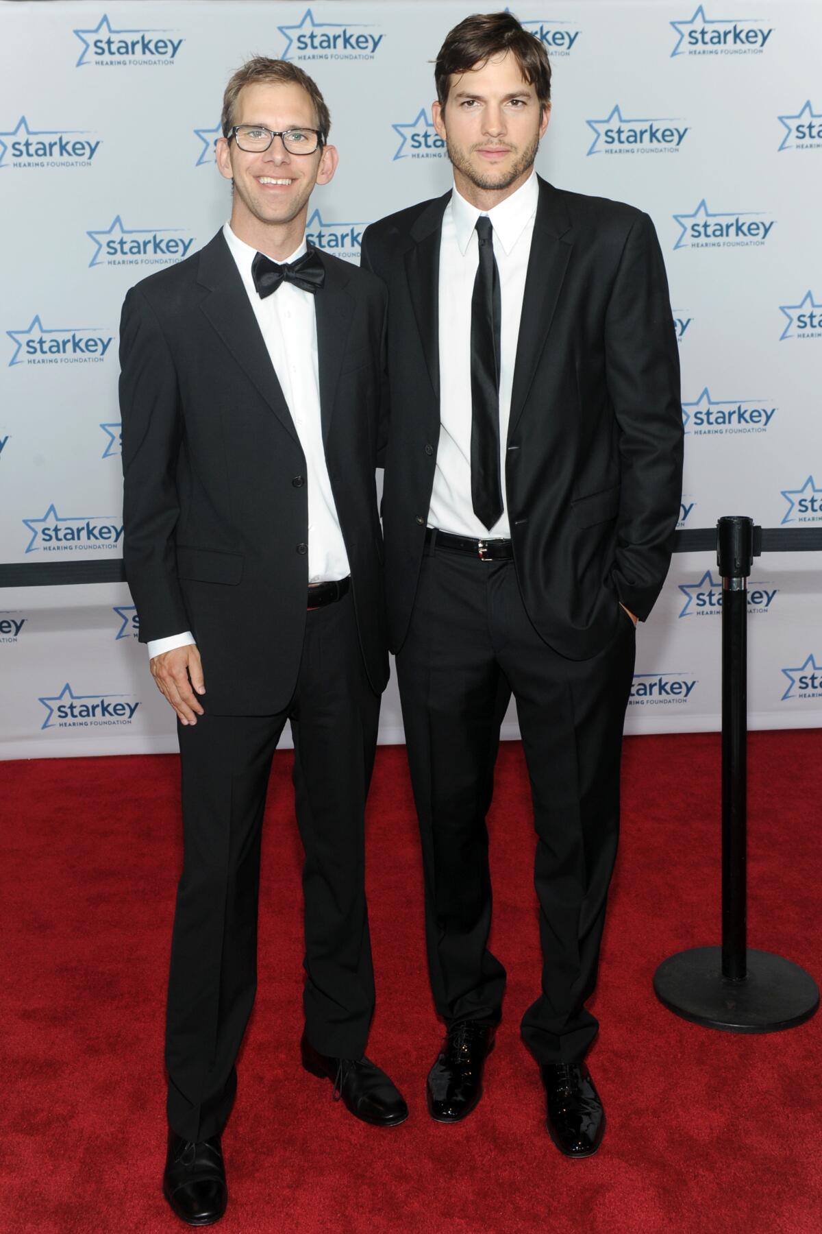 Fraternal twin brothers pose on a red carpet in tuxedos