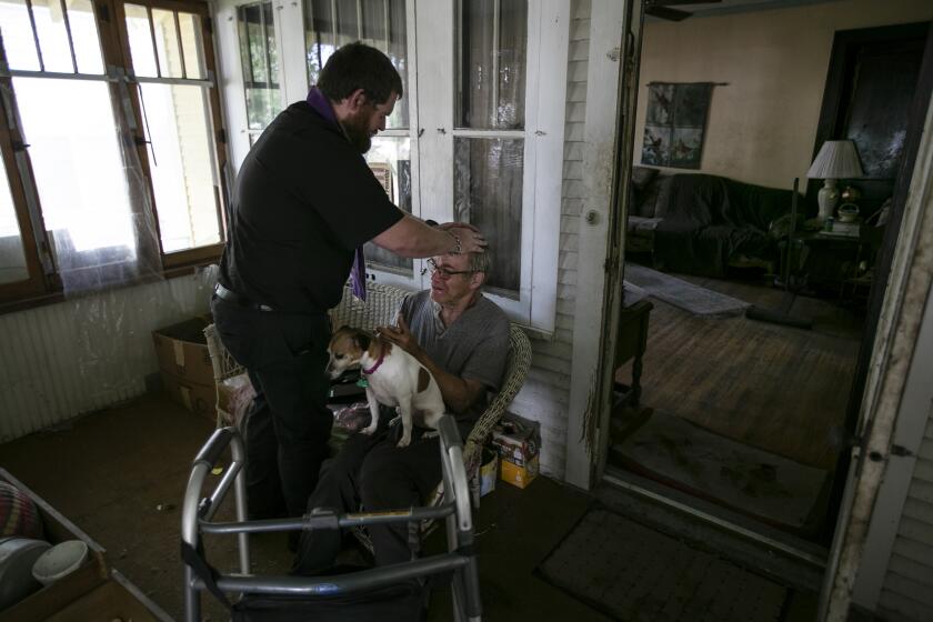 Sioux Falls, South Dakota, Friday, July 10, 2020 - Father Kristopher Cowles of Our Lady of Guadalupe Church offers a blessing to Doug Van Loh, 62 at his home as Sadie stands by. Van Loh is a long time member of the church who is now housebound. Fr. Cowles visits him regularly. (Robert Gauthier / Los Angeles Times)