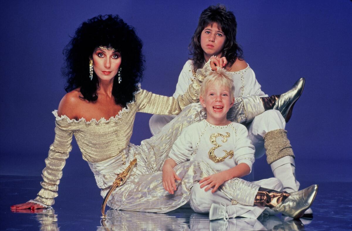 A musician/actress mother seated on the floor with her two young children, all dressed in white, in the 1980s.